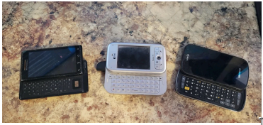 Three older mobile phones with physical QWERTY keyboards, representing pre-2007 conventional phone design