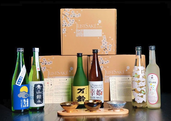 Just Sake product lineup showing sake bottles, subscription boxes with cherry blossom design, and traditional tasting bowls